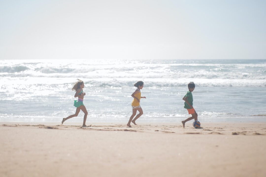 young kids from a blended family running along the beach with a ball on separate vacation